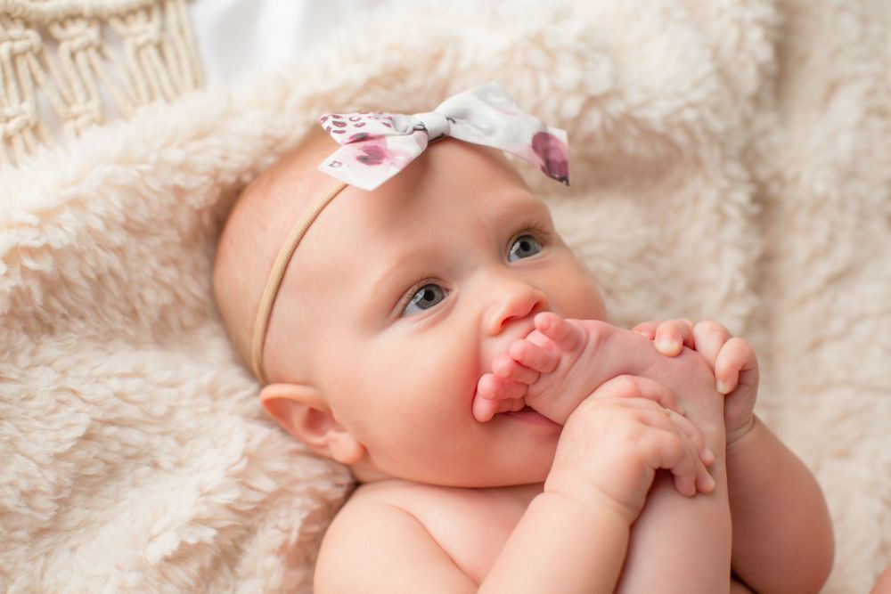 Baby wearing bow headband rests on soft beige blanket.