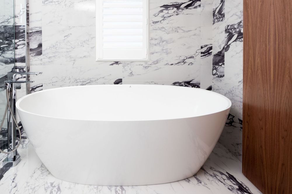 Freestanding oval white bathtub against dramatic black and white marble walls.