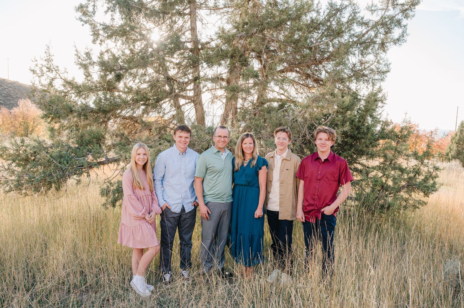 Family members stand together in a casual outdoor portrait with mountains and grass in the background.