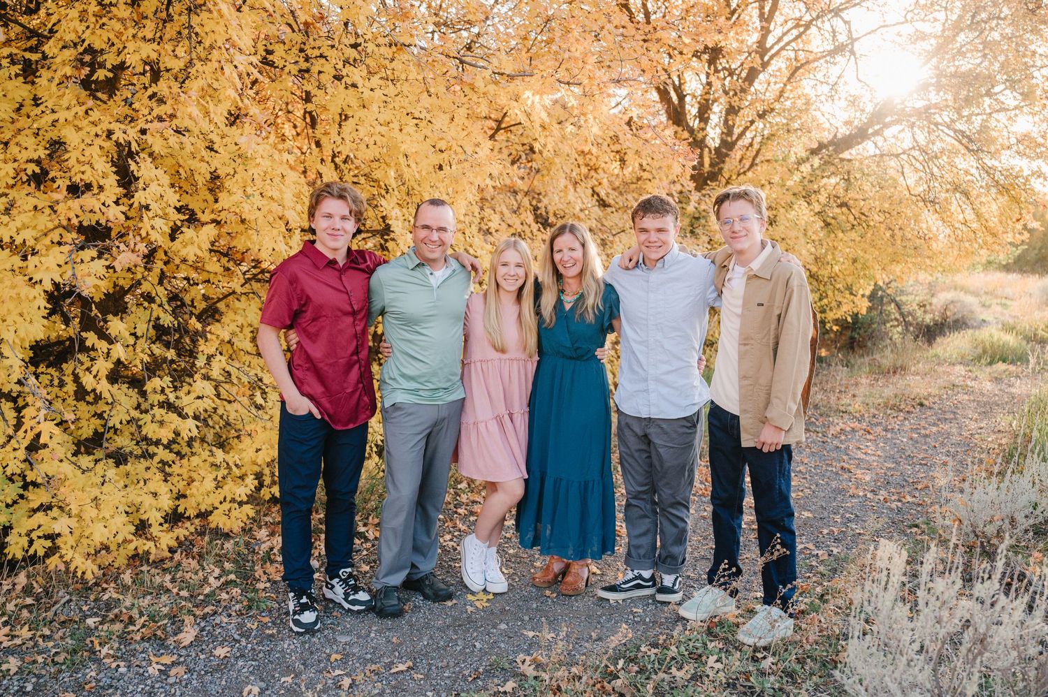 Family members gather for a portrait surrounded by golden fall foliage on a sunny day.