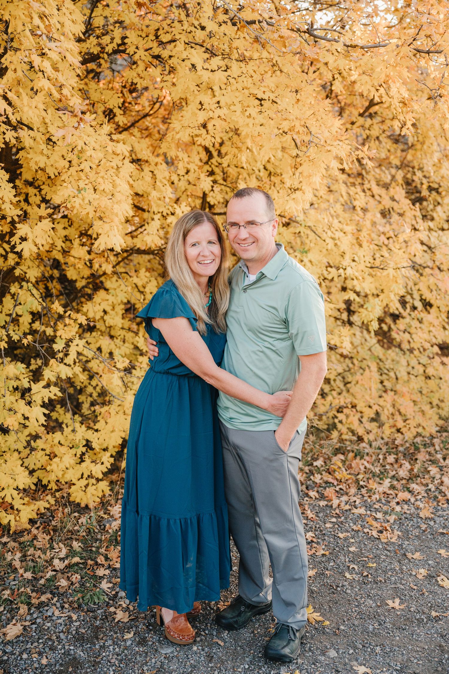 A couple poses against a golden autumn backdrop wearing coordinating blue and green outfits.