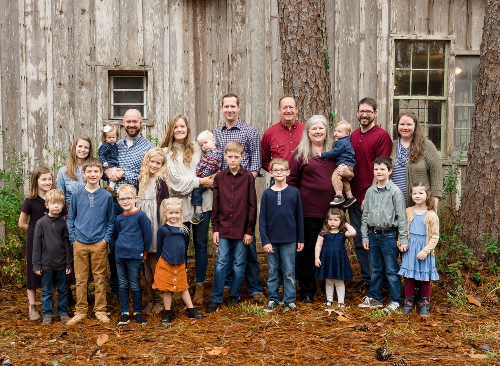 Large family group poses together in front of a rustic wooden barn wall during an outdoor photo session.