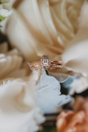 A rose gold engagement ring with diamond halo setting nestled among delicate white flowers.