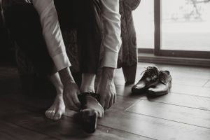 Black and white image of hands helping someone put on dress shoes on a wooden floor.