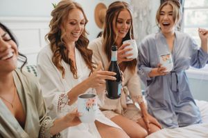 Bridesmaids in robes share laughs during wedding morning preparations.