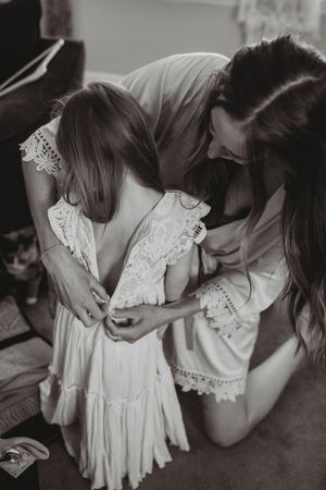 A tender moment captured in black and white as a white lace dress is adjusted.
