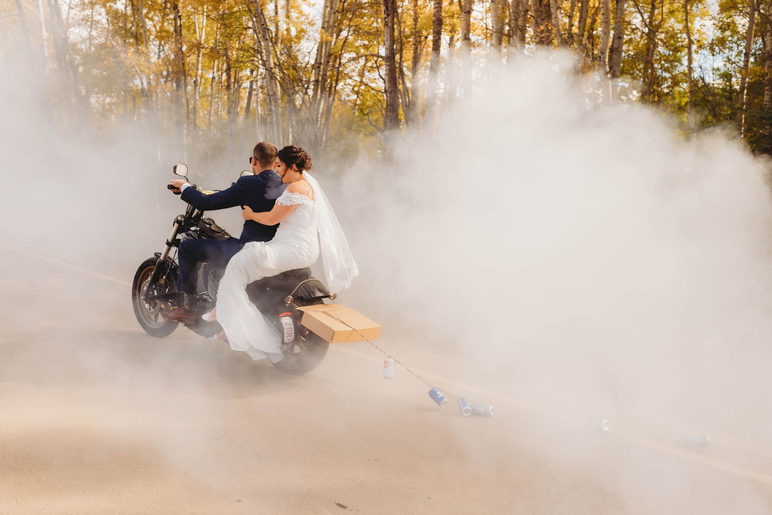A dramatic motorcycle burnout creates a cloud of smoke in an autumn forest setting.