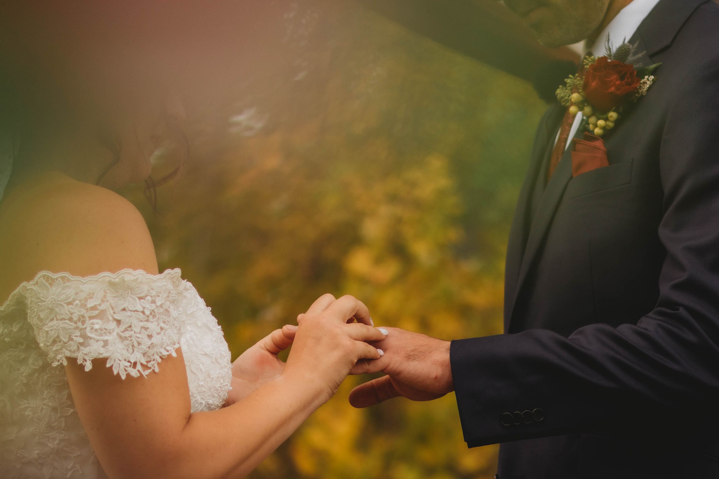 Close-up of hands exchanging wedding rings during an autumn ceremony.