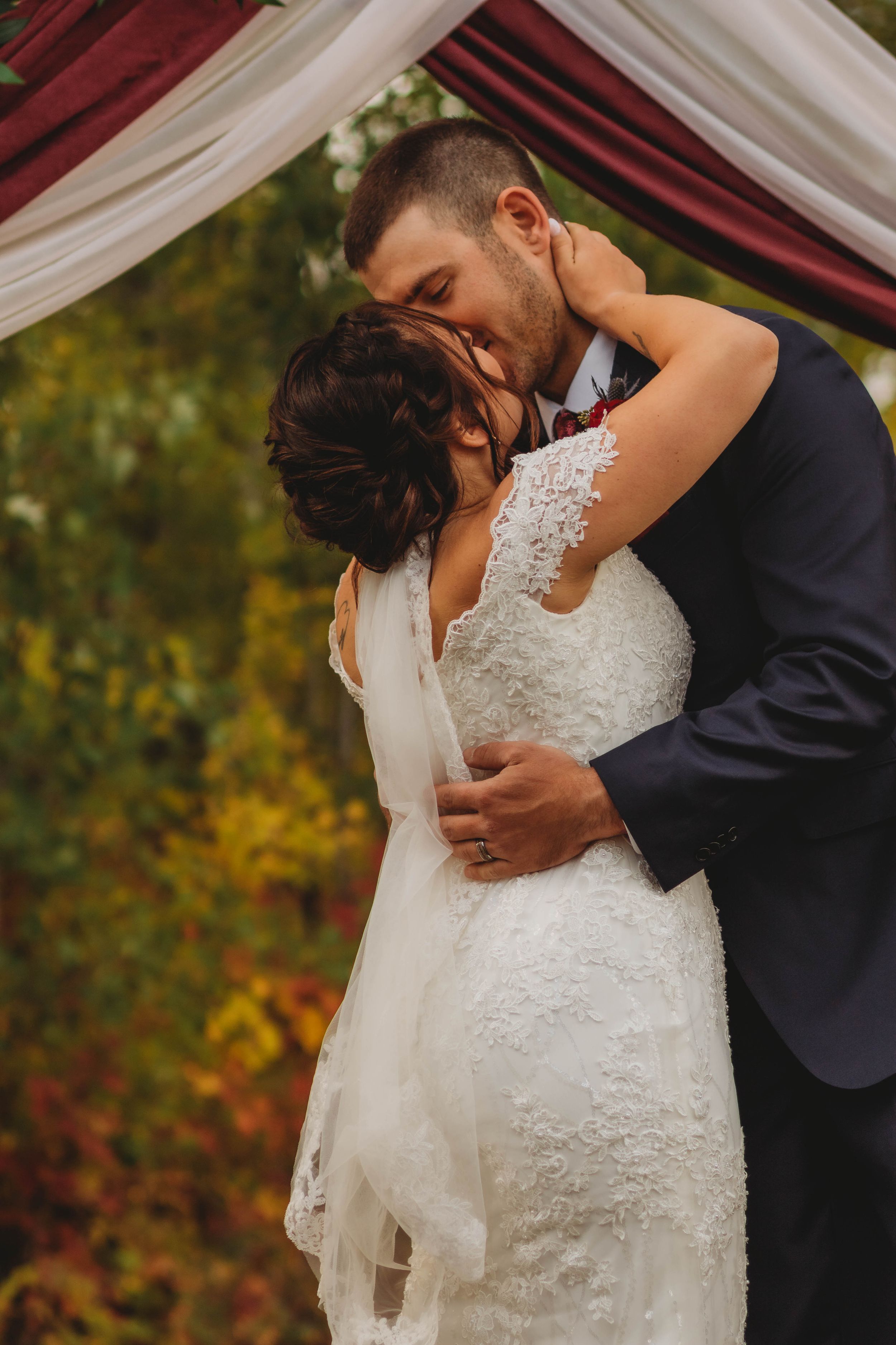 A romantic embrace under a draped wedding arch with autumn colors in the background.