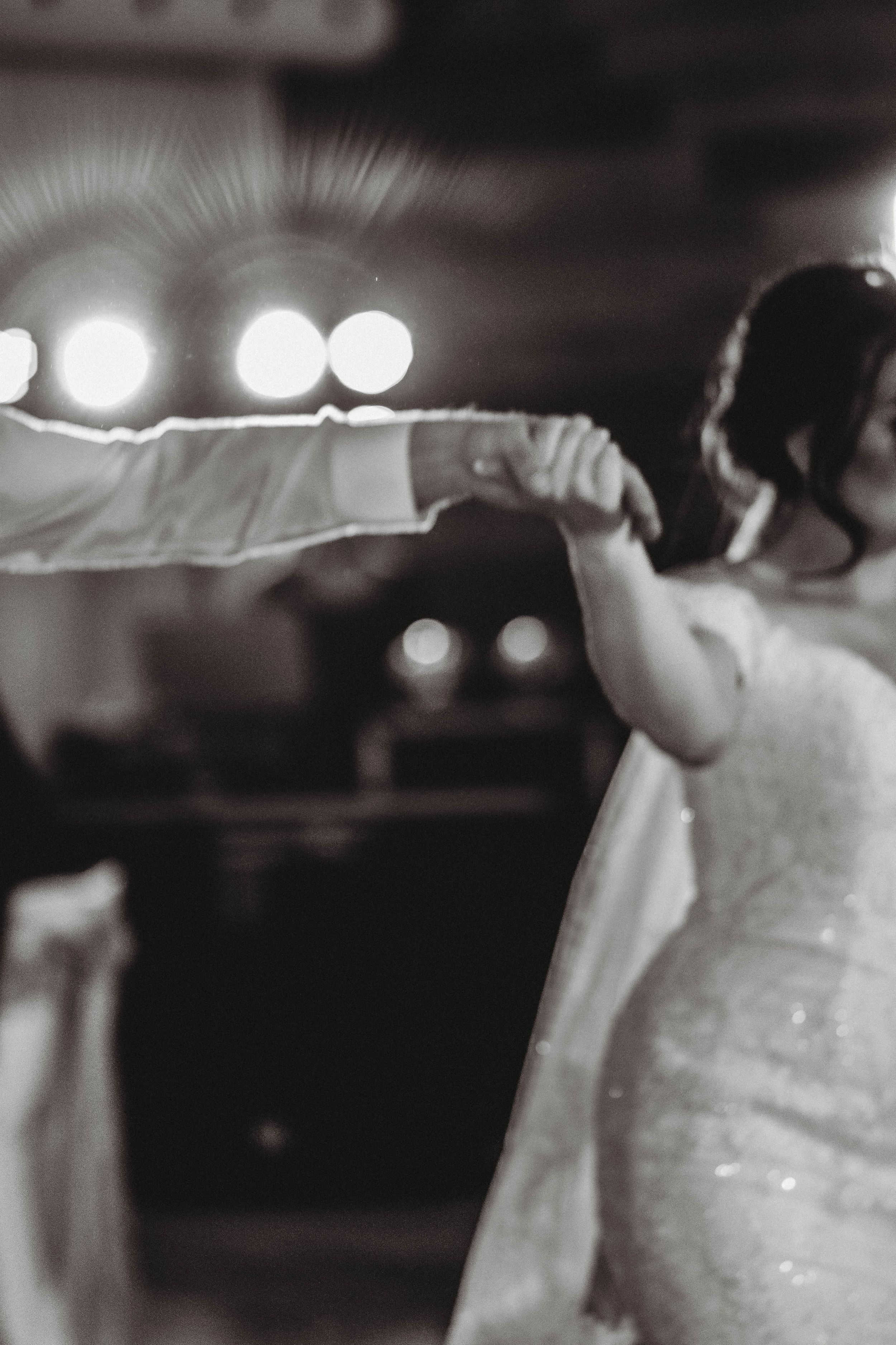 A black and white photo showing a long white veil flowing in soft focus with bokeh lights.