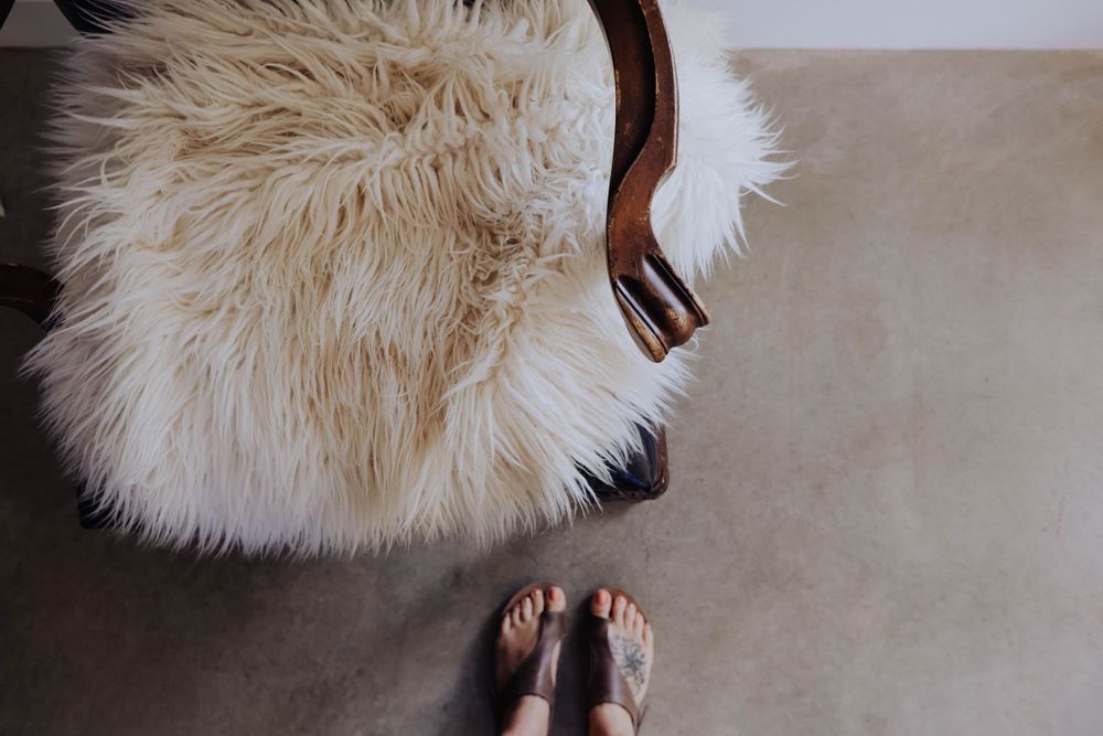 Close-up view of feet near a fluffy white sheepskin on a dark wooden chair.