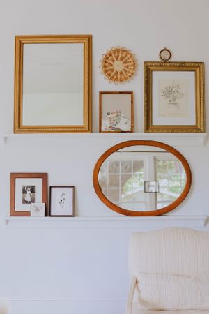 Gallery wall featuring gold frames and oval mirror arranged above white chair.