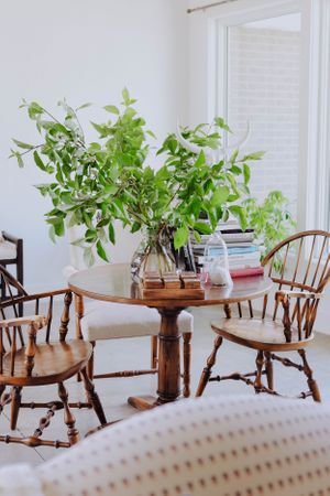 Bright dining nook with Windsor chairs and fresh greenery in glass vase on pedestal table.