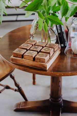 Wooden tic-tac-toe game board on round table with green plant in glass vase.