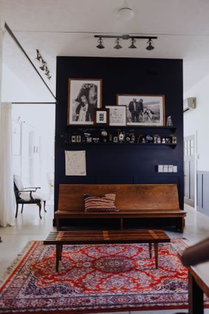Minimalist living space with wooden bench, ornate red carpet, and photo gallery wall against navy blue accent.