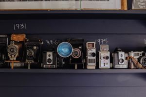 Collection of vintage cameras and photographs displayed on a dark shelf against a navy wall.