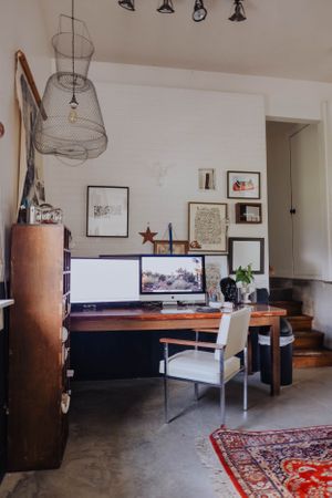 Contemporary home office space with track lighting, wooden furniture, and oriental rug on concrete floor.