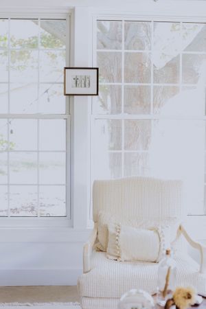 Bright sunlit room with white curtains and cream-colored armchair near windows.