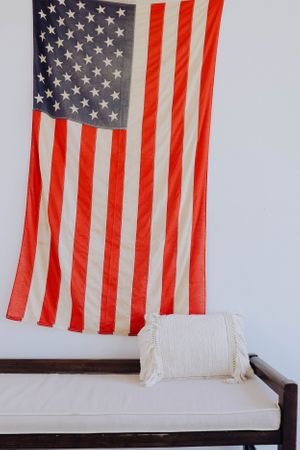 American flag displayed above a white cushioned bench against a plain wall.