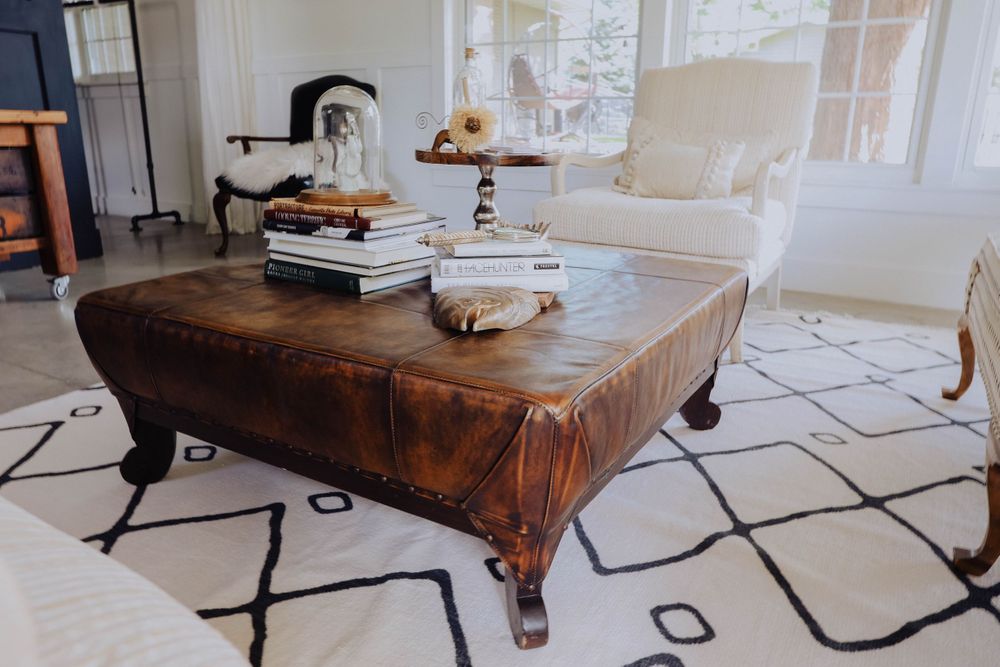 Living room featuring a brown leather ottoman and black geometric pattern rug on light flooring.