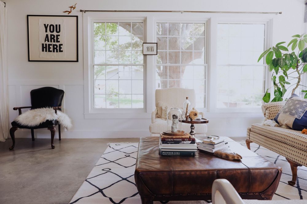 Bright living room with large windows, indoor plants, and modern furnishings in neutral tones.