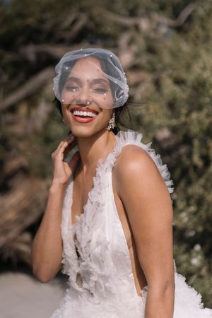 A bride in a white high-neck wedding dress and veil poses outdoors while laughing joyfully in a series of candid shots.
