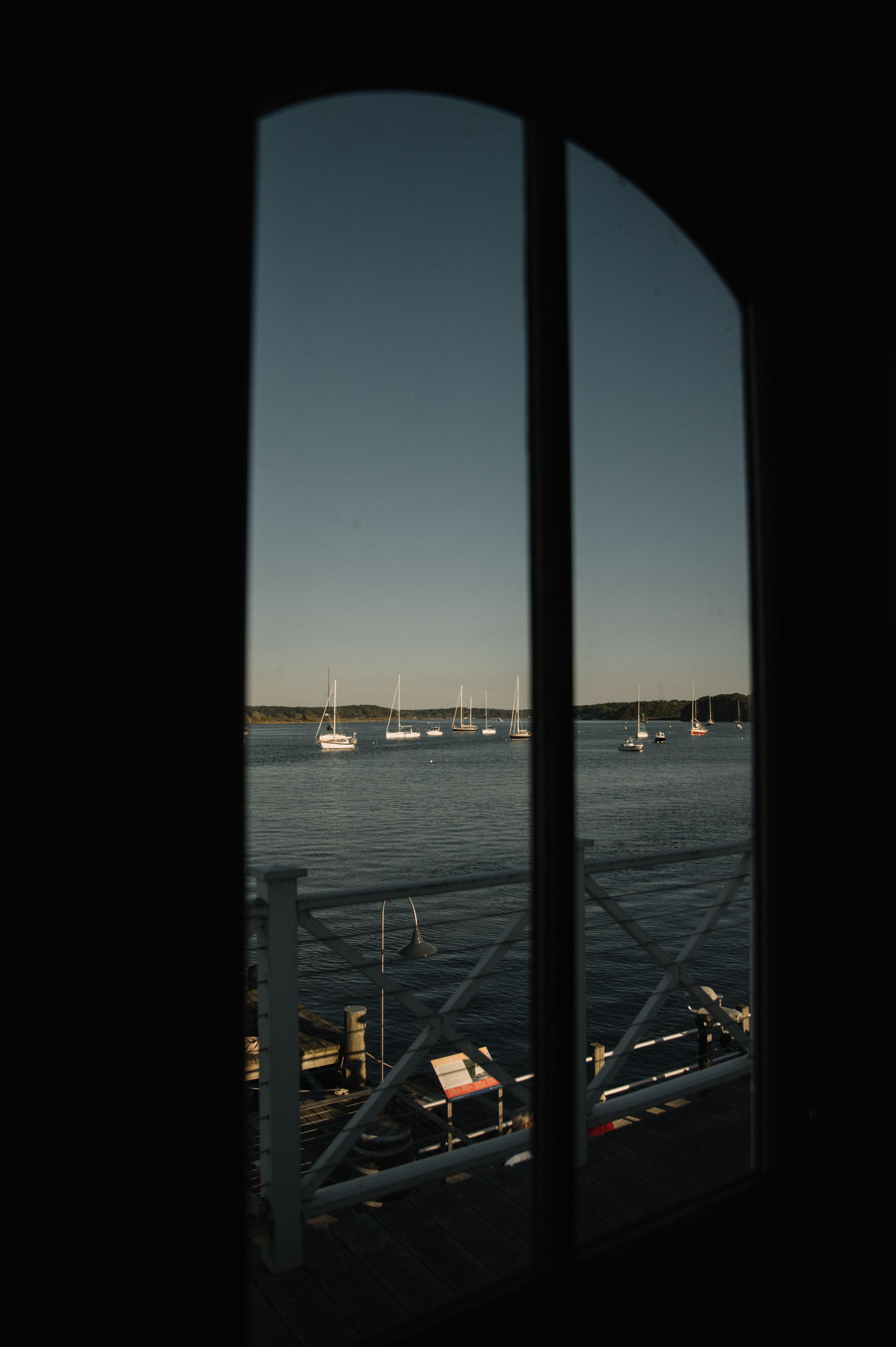 View of sailboats anchored in harbor through window frames at sunset creating silhouetted geometric shapes.