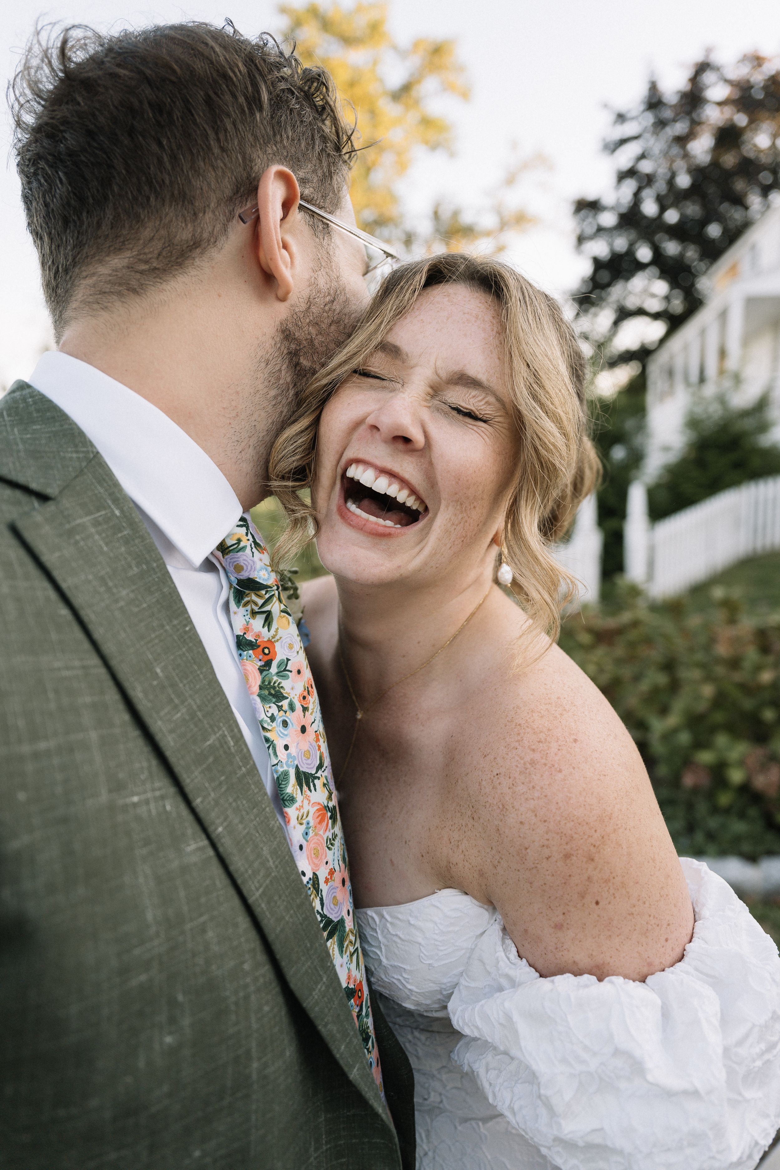 A romantic candid moment between newlyweds sharing laughter outdoors with natural lighting.