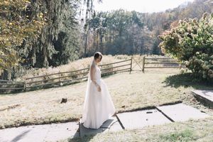 A figure in a flowing white wedding dress stands on stone steps overlooking a rustic fenced garden in autumn.
