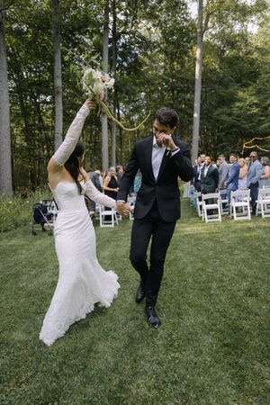 A couple performs a fun twirling dance move on a grassy lawn with white chairs and trees in the background.