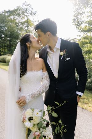 A romantic wedding couple shares intimate kisses in a sunlit outdoor setting with lush greenery and natural light.