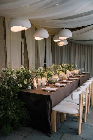 Elegant wedding reception table with modern dome pendant lights, dark tablecloth, and lush greenery centerpieces.