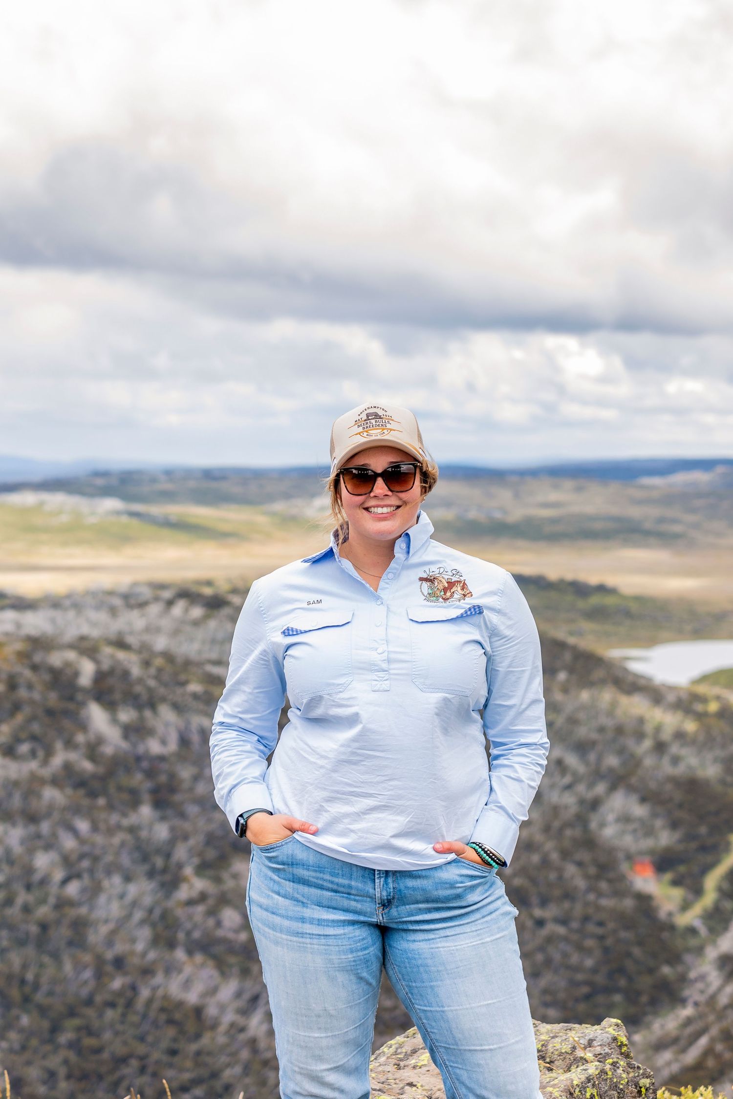 A person in casual attire standing on rocky overlook with scenic mountain vista behind.
