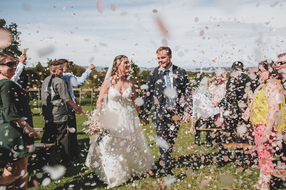 Wedding party celebrates outdoors with confetti flying through the air during a festive moment.