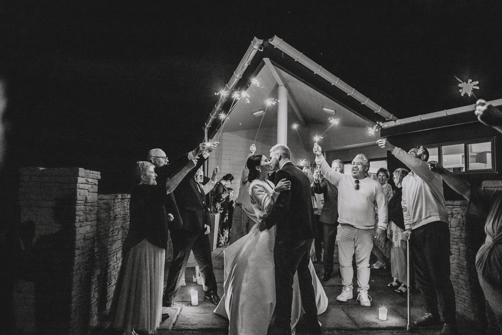 Black and white photo of wedding reception guests celebrating under outdoor lighting at night.