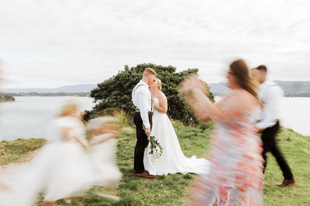 Motion-blurred wedding celebration by the ocean with guests dancing in the foreground.