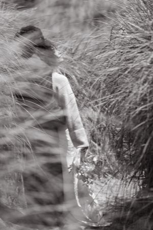 A blurred black and white artistic photograph showing newlyweds among tall grass swaying in the wind.