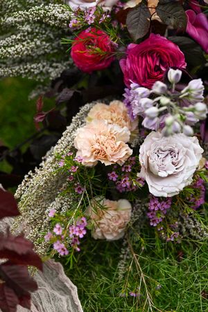 Close-up of lush floral arrangement with pink roses, white carnations, and delicate baby's breath against greenery.