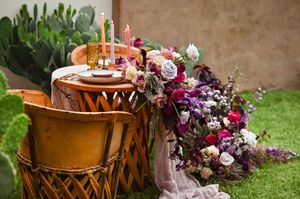 Rustic wooden sweetheart table and chairs sit in a garden setting with vibrant floral arrangements on display.