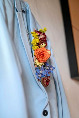 A delicate flower corsage with roses and blue hydrangeas pinned to a light blue suit jacket.