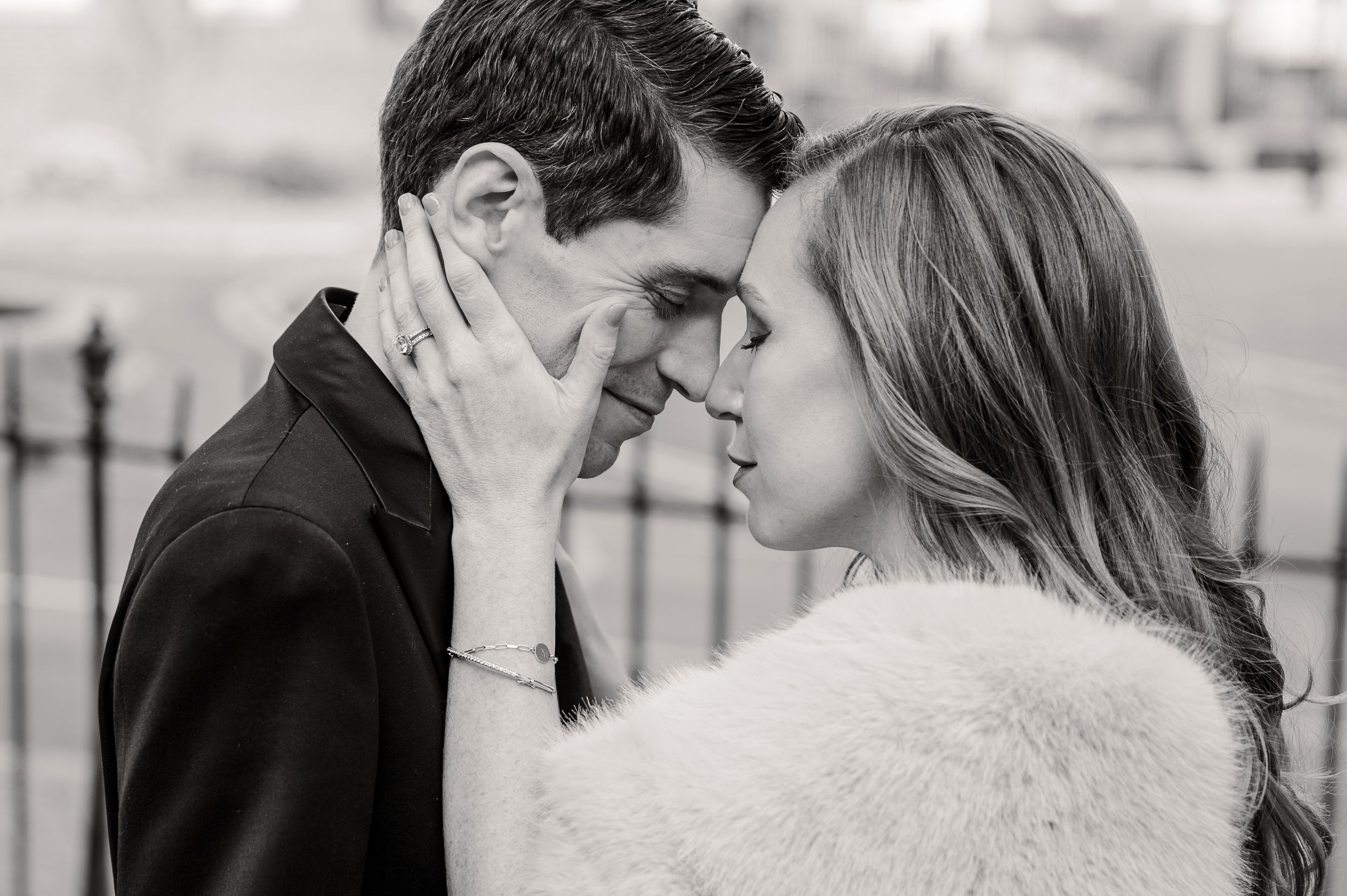 Black and white photo of a romantic couple touching foreheads tenderly outdoors.