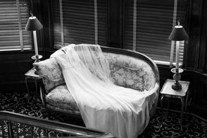 Black and white photo of an elegant bridal gown draped over an ornate vintage sofa flanked by two table lamps.