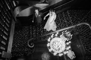 Aerial black and white view of bride and groom descending grand staircase with ornate chandelier below in Baltimore.