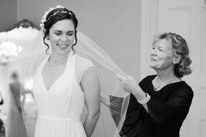 Black and white photo of a bride smiling as an older woman adjusts her wedding veil.