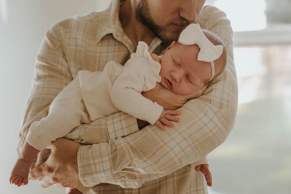 A tender moment captured in soft white clothing against a bright window.