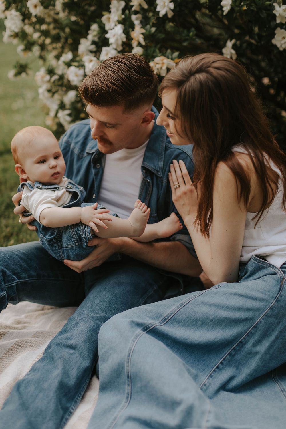 Intimate family moment sitting on a blanket outdoors with blooming flowers in the background.