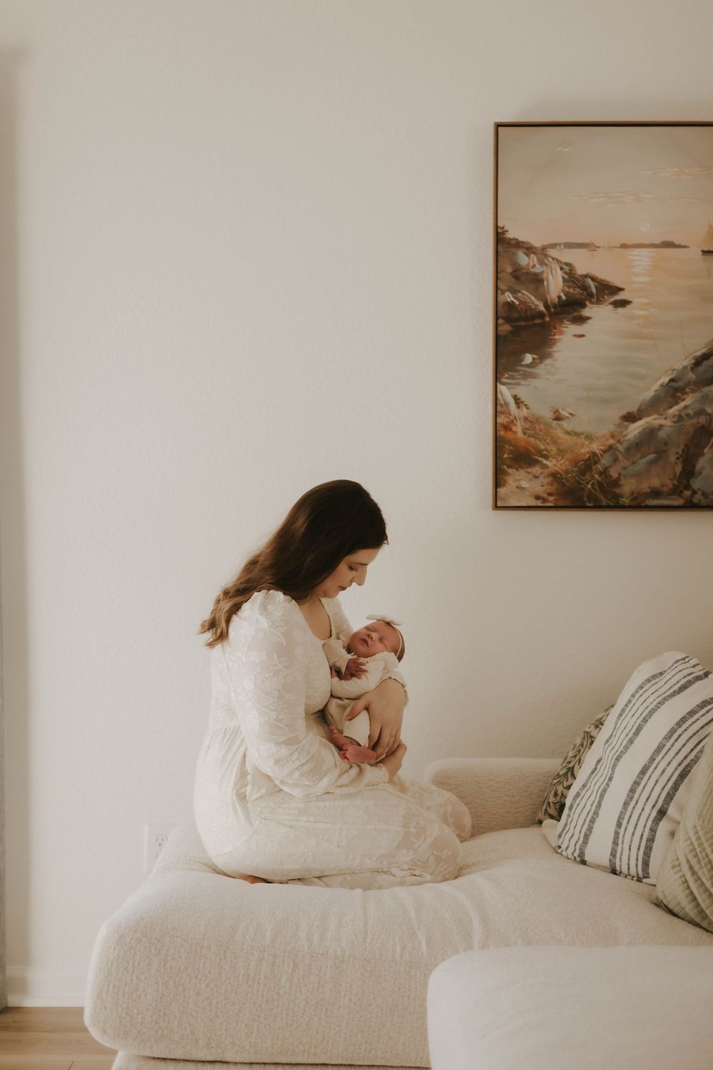 A peaceful moment with mother and newborn on a white couch with artwork in the background.