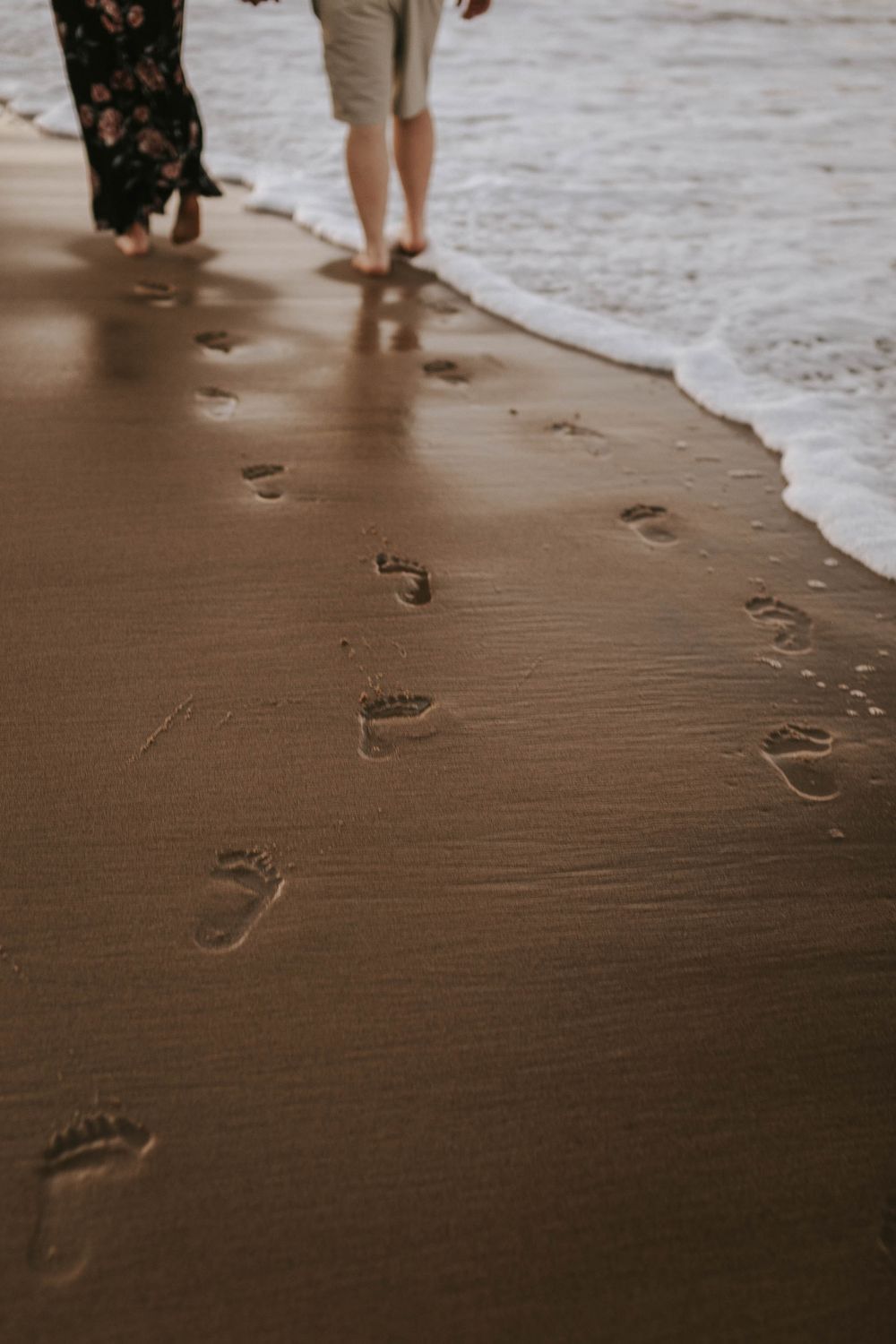 Footprints in wet sand along beach shoreline during family photoshoot.