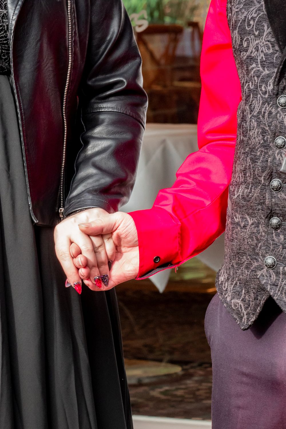 Bride in black dress and groom in black vest in Close-up of hands clasped together during a wedding ceremony.