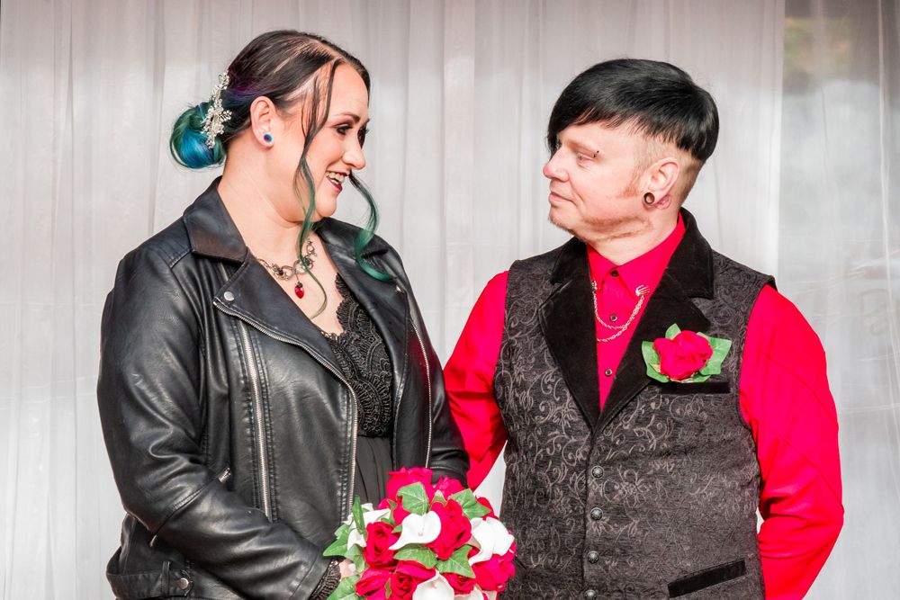 Bride in black dress and groom in black vest share an intimate moment at a wedding ceremony.